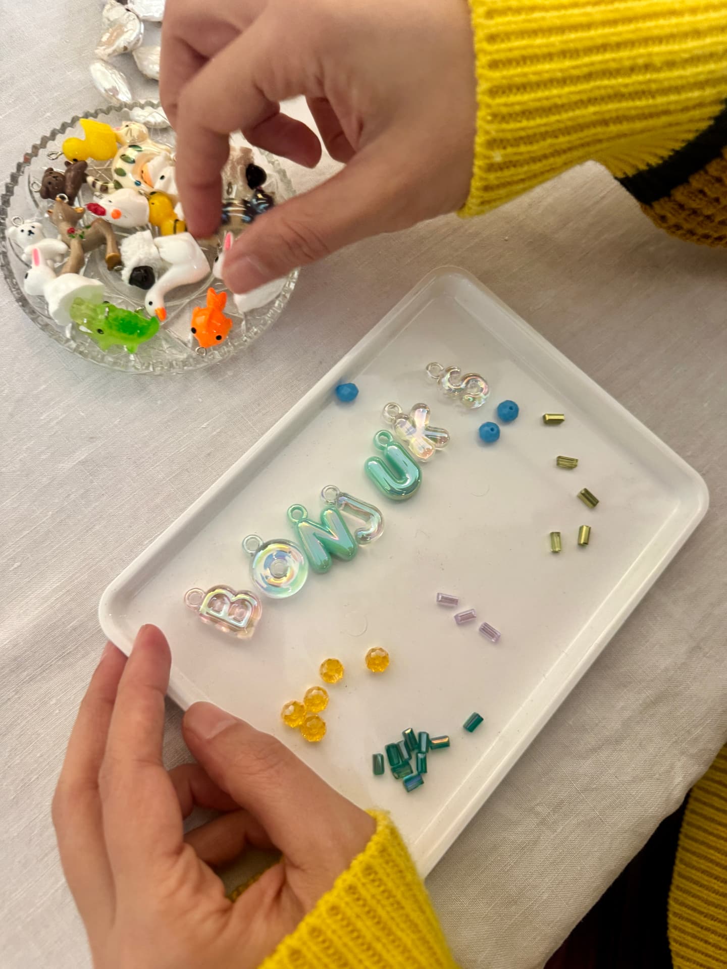 Hands arranging charms and beads on a white tray